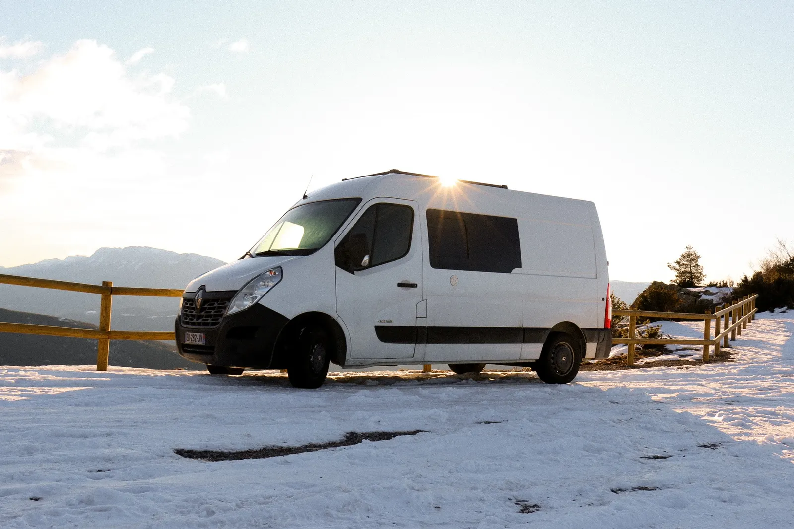 Isaac, un Renault Master blanc aménagé, garé sur un parking enneigé en montagne