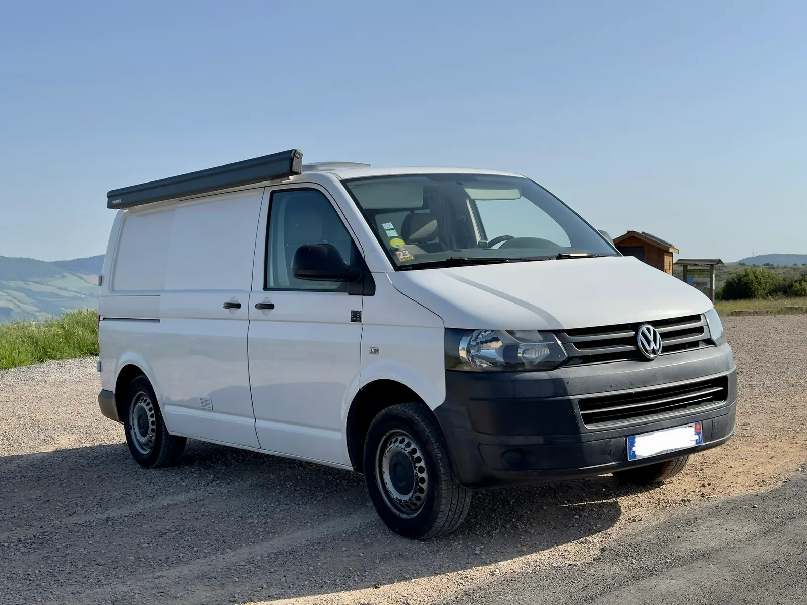 Jane, un Volkswagen T5 blanc aménagé, vu de trois quarts avant sur un chemin