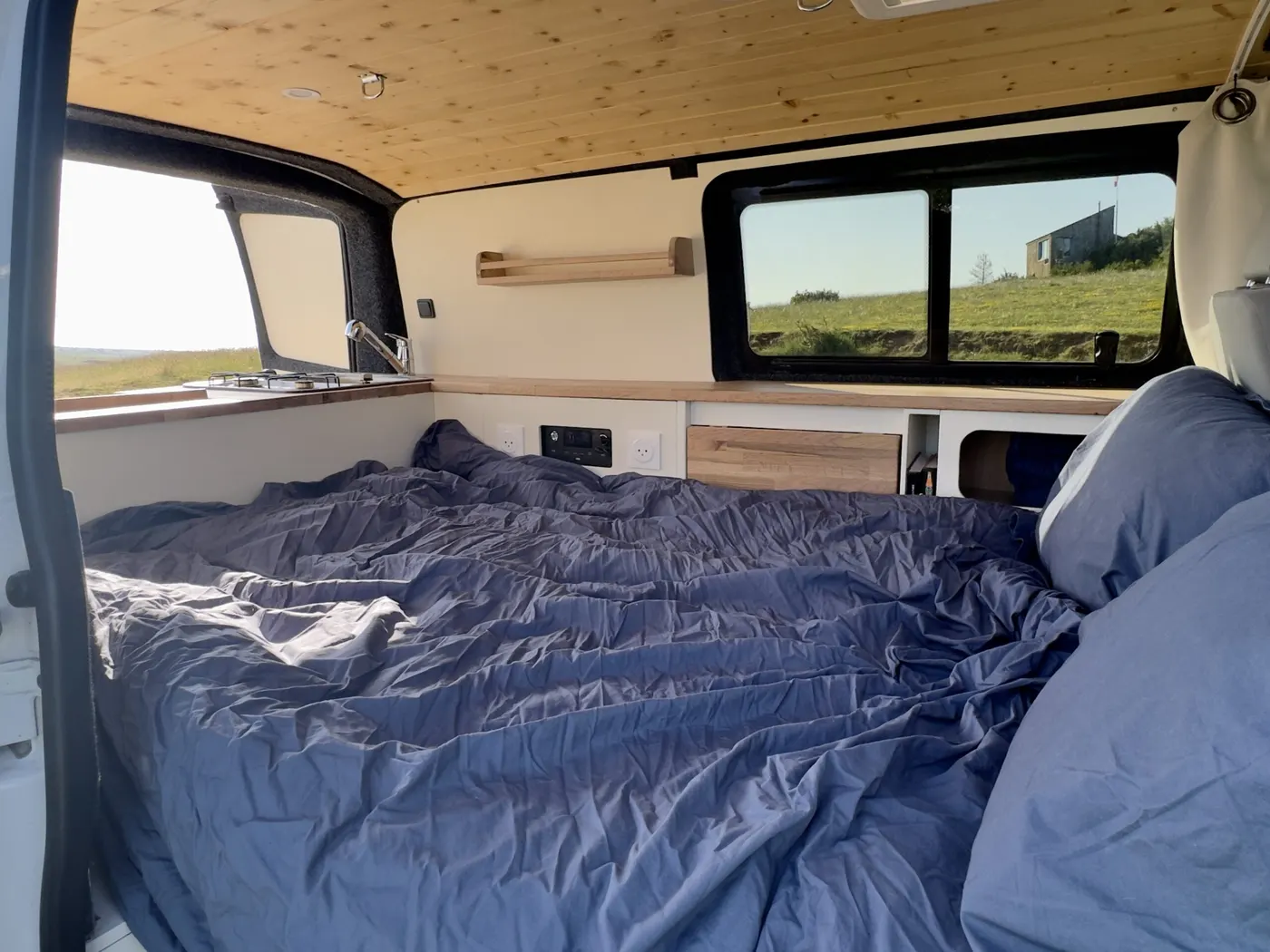 Le lit de Jane déplié en 120 × 190 cm, draps bleus, vue sur la campagne par la fenêtre