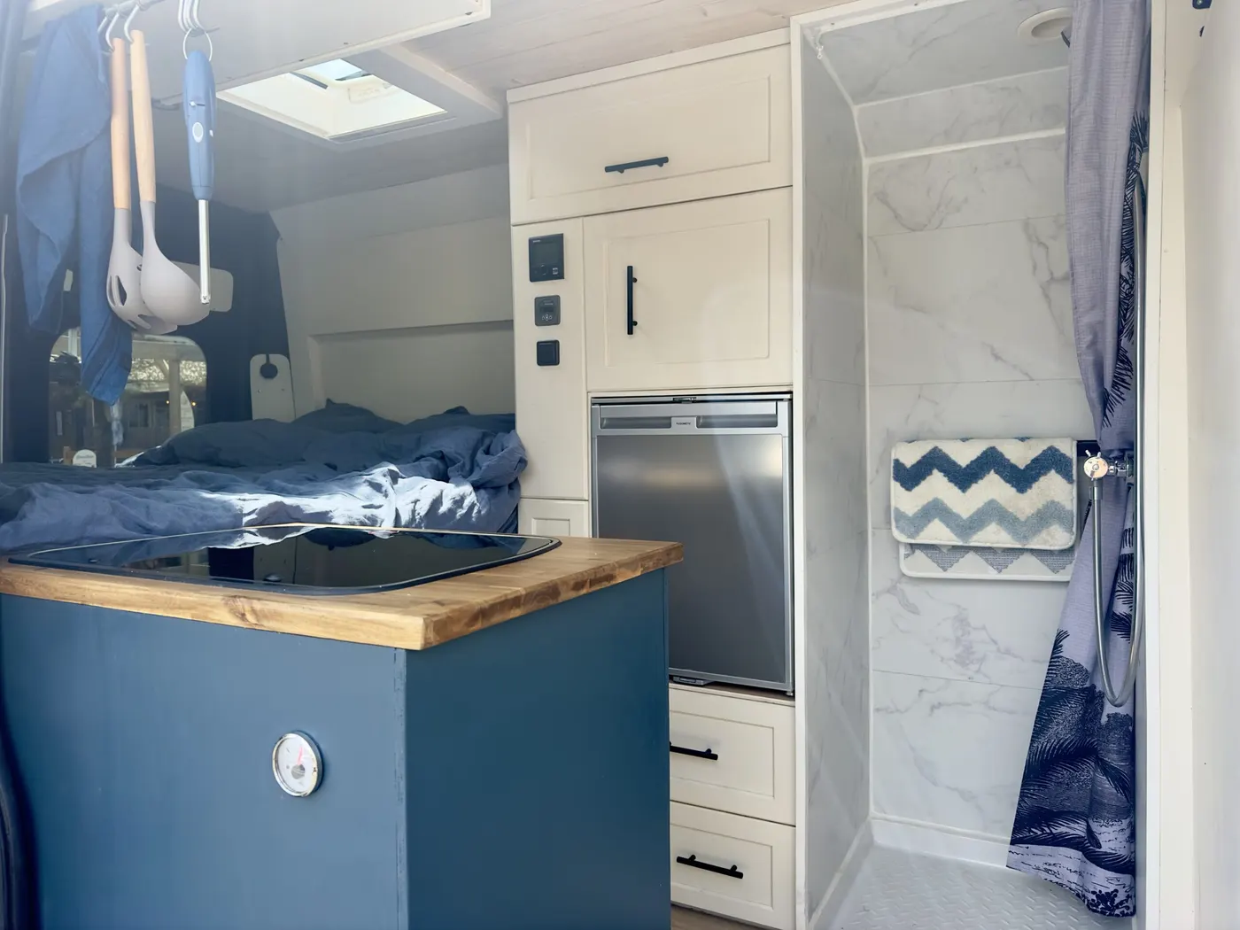 Intérieur de Léonard, porte de la cabine de douche ouverte, cuisine bleue au premier plan