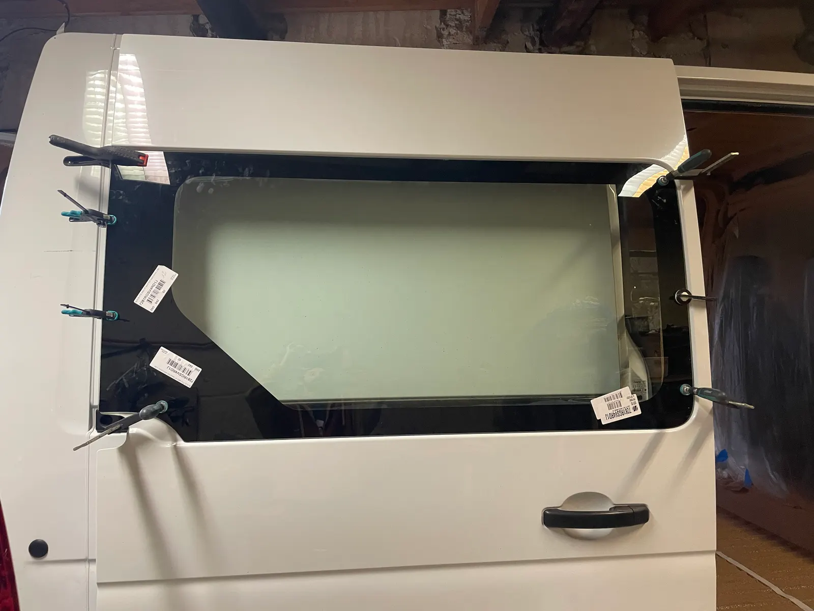 Fenêtre collée sur la porte latérale d'un fourgon blanc, maintenue par une dizaine de serre-joints pendant le séchage