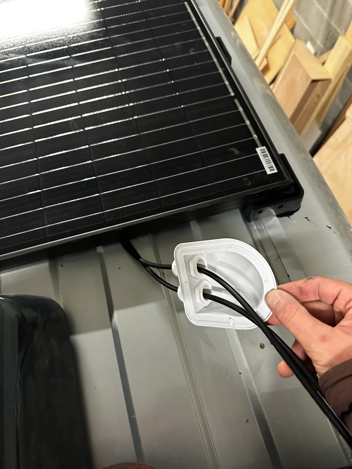 Main qui présente un passe-câble blanc sur le toit d'un fourgon, à côté d'un panneau solaire noir